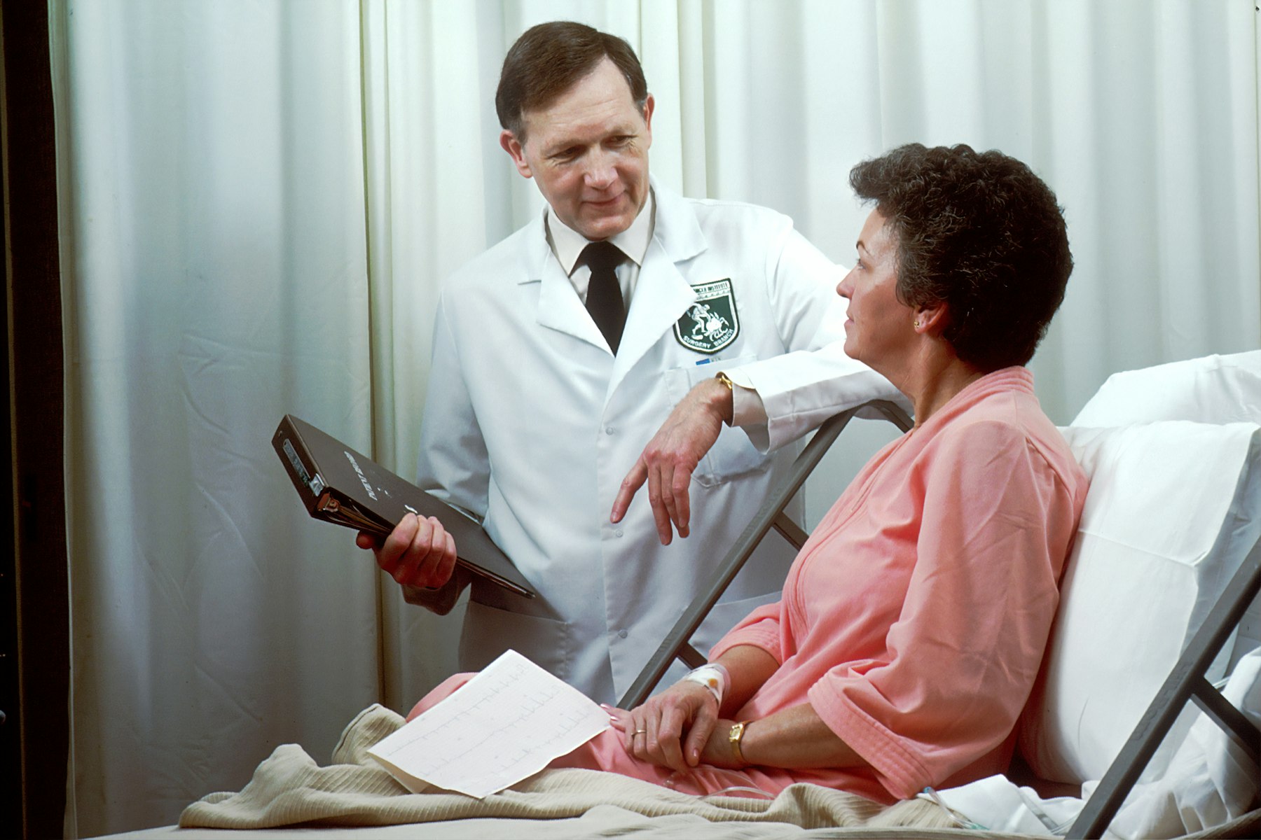 Cardiologist talking with a woman resting in a hospital bed after a heart procedure